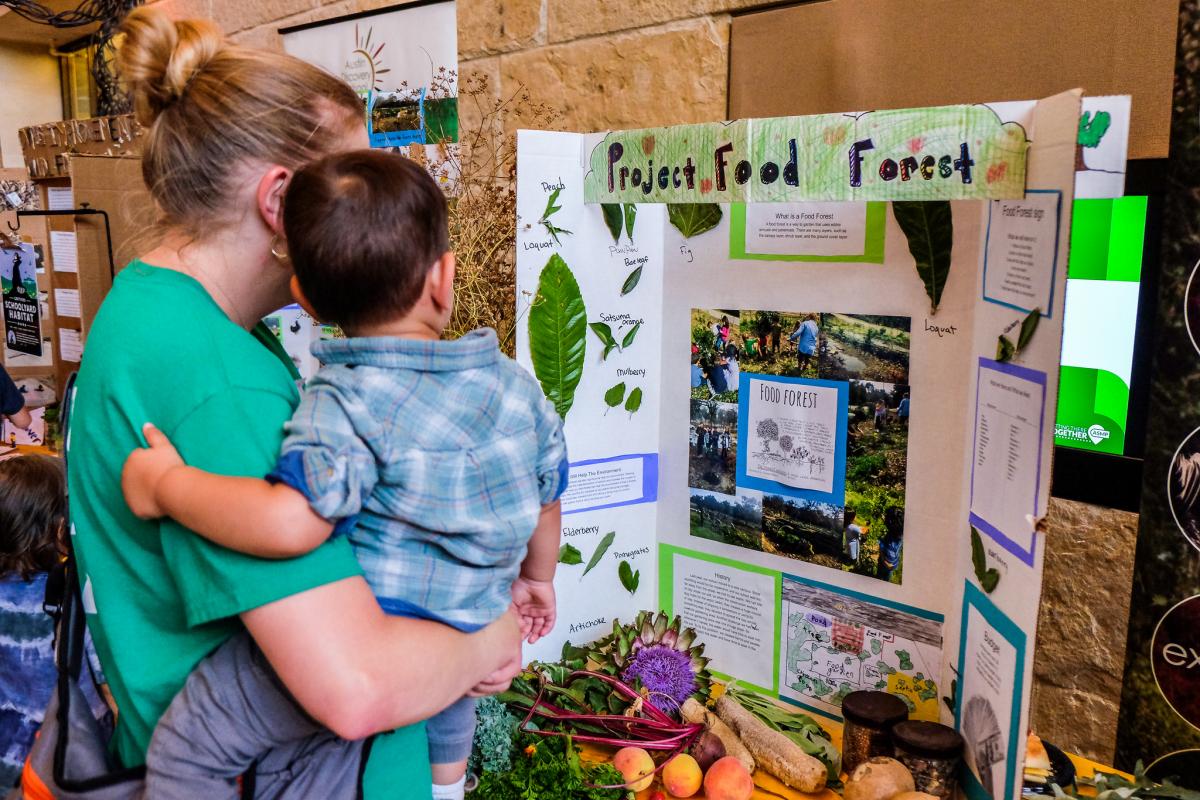 Mom and child looking at a student project display board titled "Project Food Forest"