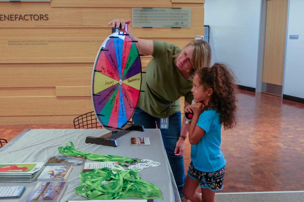 Mary Priddy showing a little kid how to spin a prize wheel.
