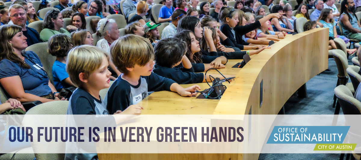 Text reads "Our future is in very green hands" overlay on photo of kids sitting at long wooden desk in Austin City Council Chambers