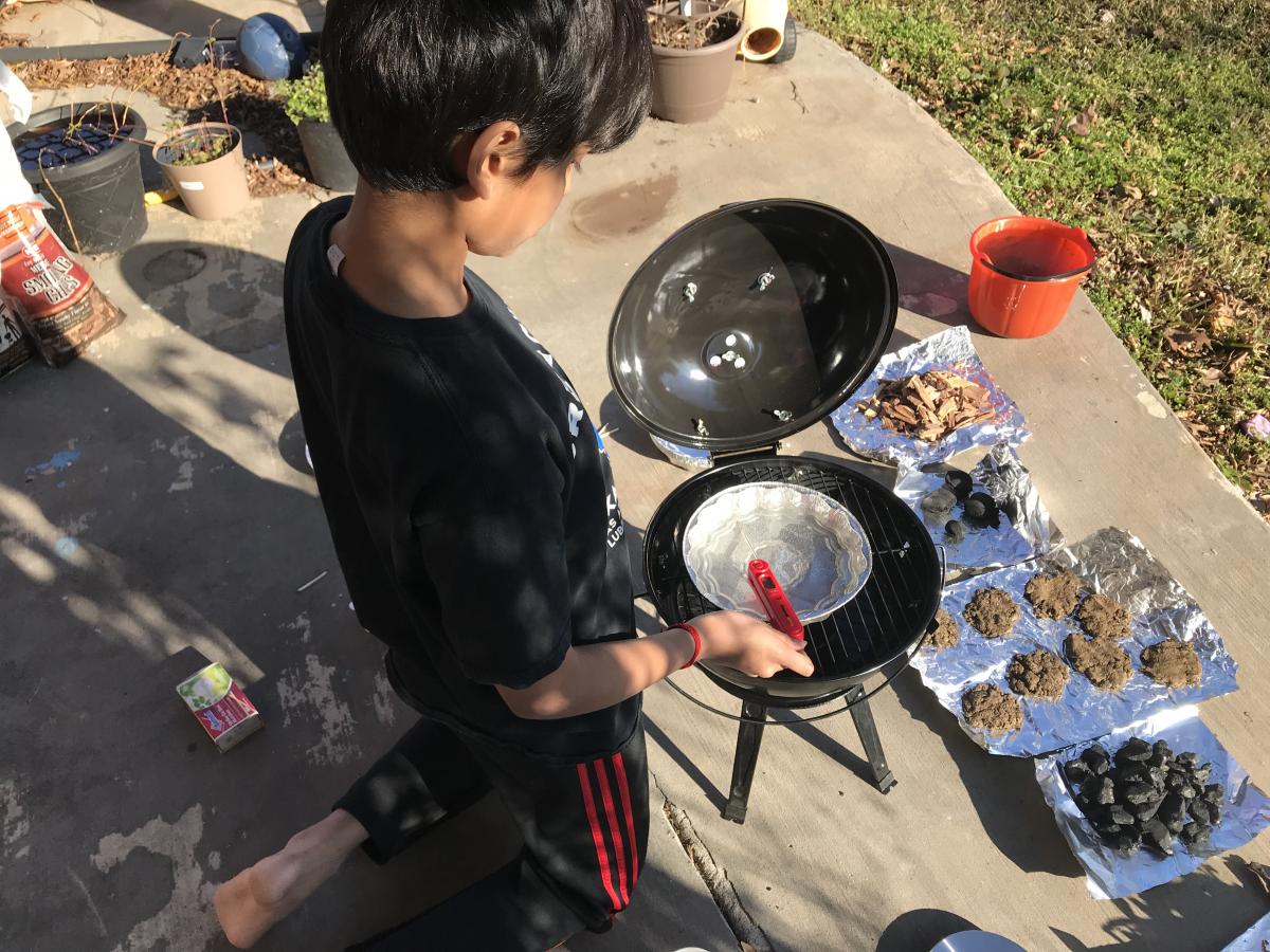 Pranav kneeling over fire pit with his materials for the experiment.