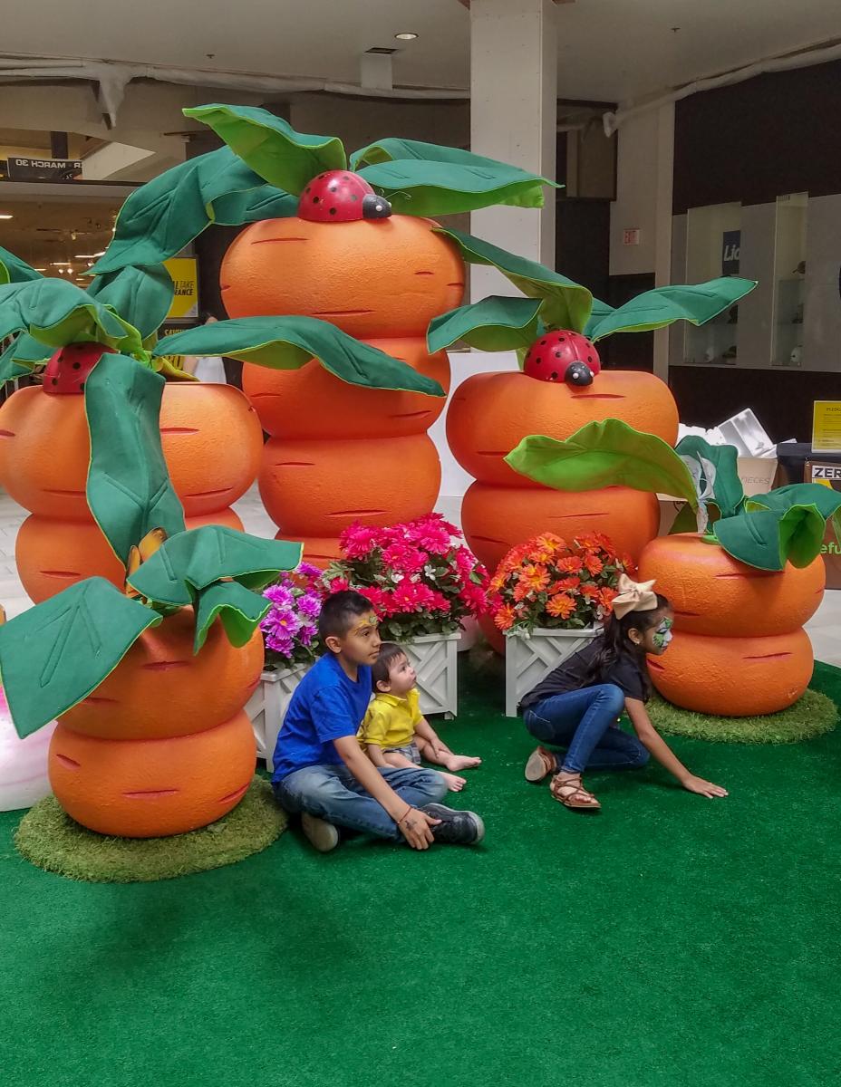 Kids taking a picture in front of large orange carrots.