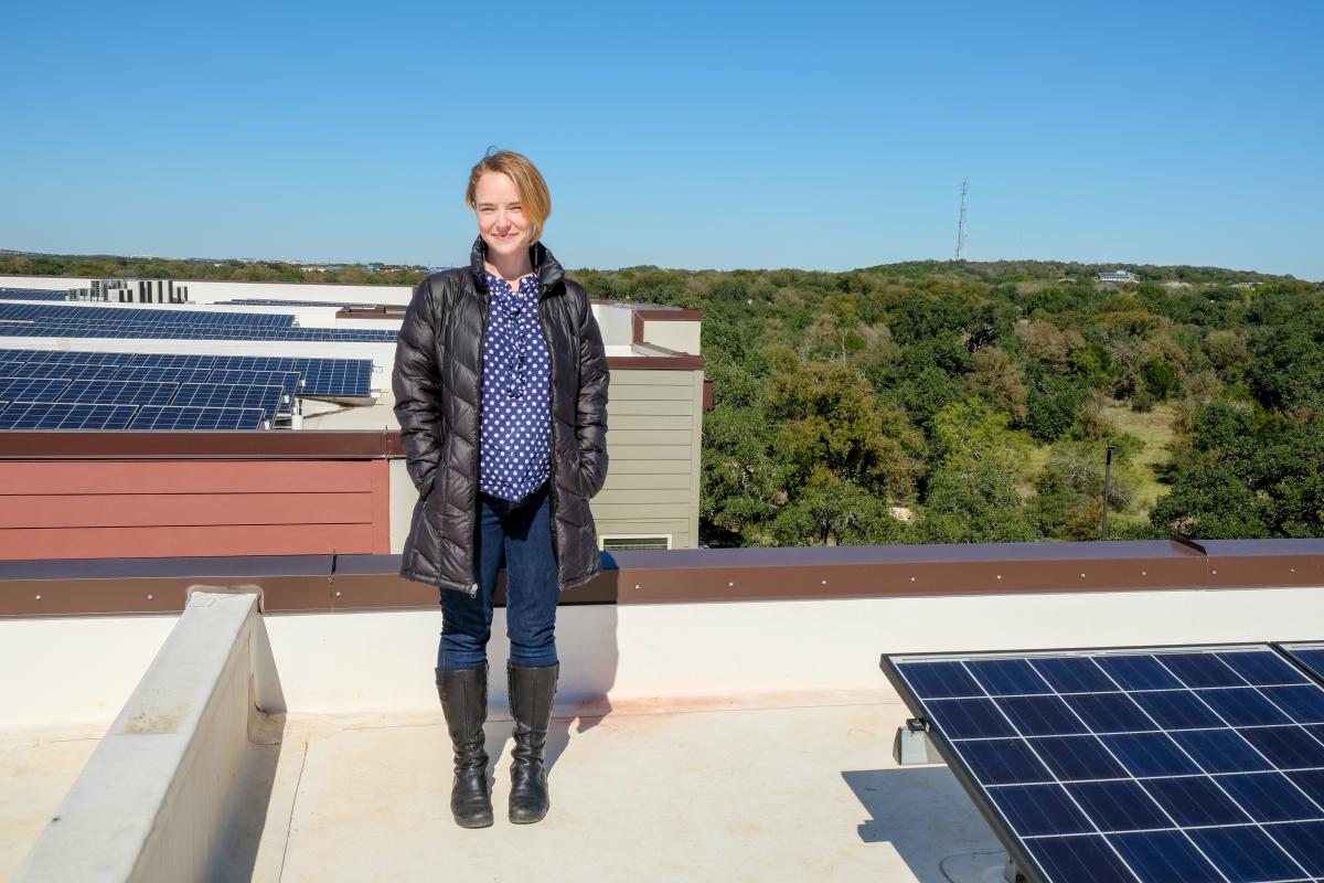 Susan Peterson standing on a rooftop. There are solar panels around her and a view of the hill country to her right.
